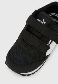 Μαύρο παπούτσι Puma για νήπια με λευκές λωρίδες λογότυπου και δύο ιμάντες βέλκρο σε λευκό φόντο.