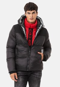 Schwarze Daunenjacke mit einer roten isolierten Innenschicht, ausgestattet mit einer Logo-betonten Kapuze, Reißverschluss, Fronttaschen und gerippten Ärmelbündchen.