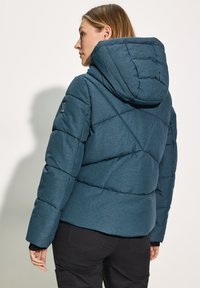 Teal kleurige pufferjas met capuchon, met een gewatteerd ontwerp en een gestructureerde afwerking. Inclusief een logo op de linker mouw en zwarte accenten.