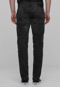 Mustat denim-farkut slim fit -mallilla, joissa on takataskut ja minimalistinen muotoilu. Yhdistetty mustiin kenkiin ja ketjukoruseen.
