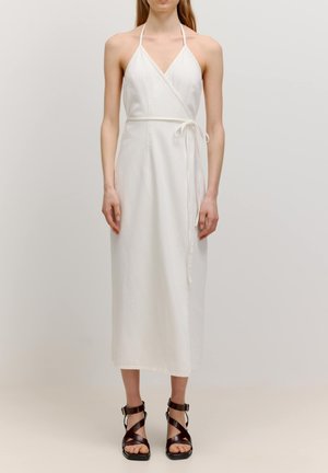 Weißes Halfter-Wickelkleid mit schmaler Passform, Taillenschnürung und langem Schnitt. Glatter Stoff mit schlichtem Design und ohne sichtbare Muster. Braune Sandalen.