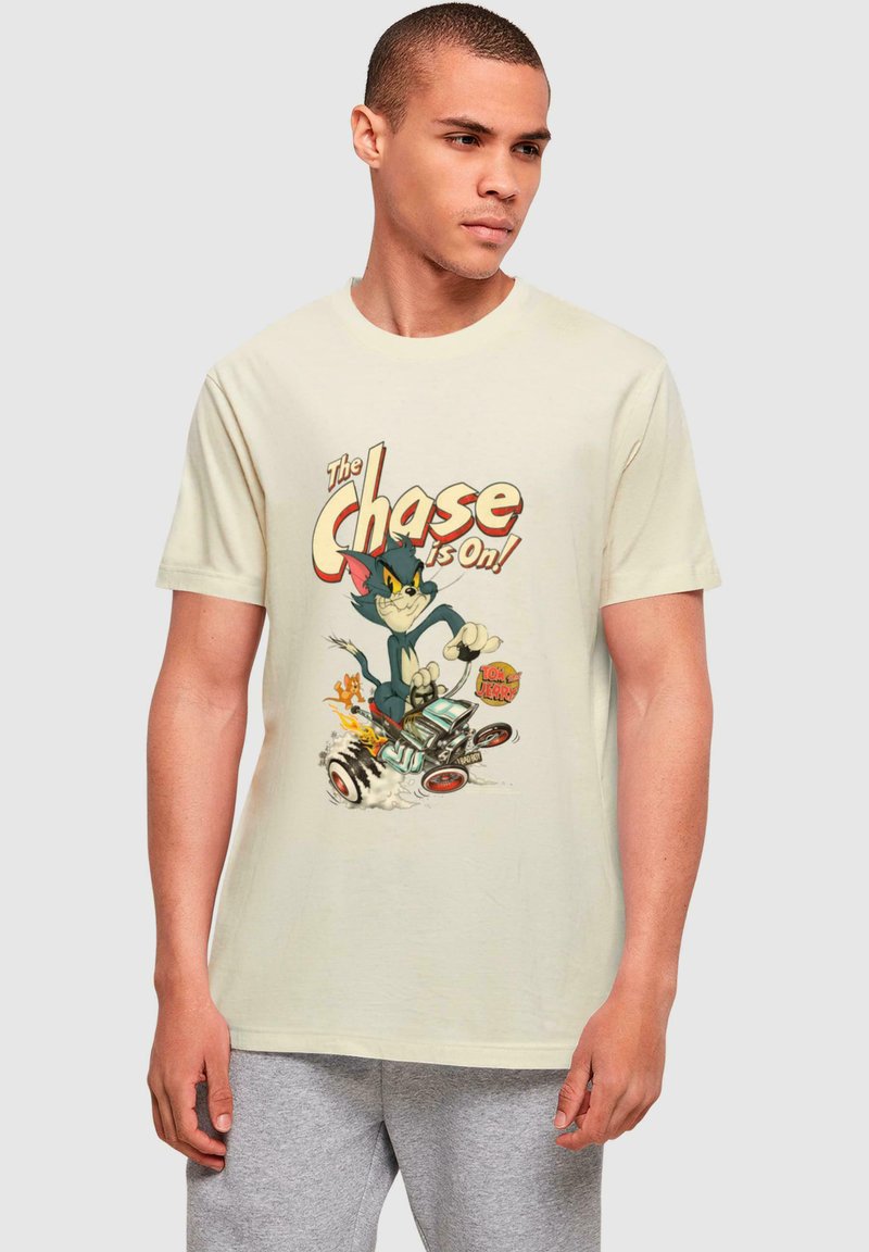 Beige bomulds t-shirt med et tegneserieprint af en blå kat og en brun mus i en racerbils, med farverig tekst der siger "Jagten er i gang!"