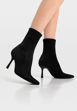 Schwarze Knöchelstiefel mit schlankem, eng anliegendem Design, spitzer Zehenpartie und dünnem Stiletto-Absatz; gefertigt aus glattem Stoff mit mattem Finish.