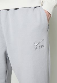 Ljust grå Nike-sweatpants med en broderad "AIR"-logga i matchande grå, sidofickor och en mjuk, texturerad yta.