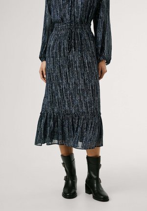 Lang, donkerblauwe jurk met verticale strepen en een gerimpelde zoom. Heeft een elastische taille en lange pofmouwen, gecombineerd met zwarte enkellaarzen.