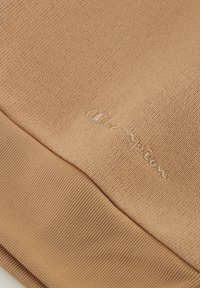 Material de suéter de algodón marrón con tejido texturizado y dobladillo acanalado. Presenta un sutil logotipo bordado de "Champion" en hilo a juego.