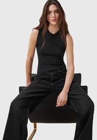 Sort ærmeløs top i en tætsiddende design parret med løse sorte jeans, der har høj talje og klassisk fem-lommeløsning.