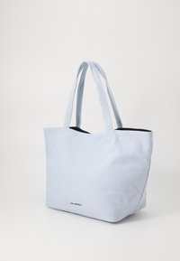 Sac en toile bleu clair avec deux longues sangles, présentant un intérieur noir et un petit logo en bas. Forme rectangulaire et design simple.