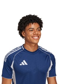 T-shirt sportivo blu con dettagli bianchi, maniche corte e colletto girocollo. Presenta un logo con tre strisce sulle spalle e sul davanti.