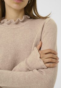 Světle růžový pletený svetr s volánovým výstřihem, dlouhými rukávy s ribbovanými manžetami a měkkým, texturovaným povrchem.