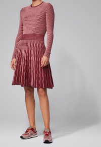 Robe en maille bordeaux avec motifs géométriques, manches longues et corsage ajusté s'évasant en une jupe plissée, assortie à des baskets rouge clair.