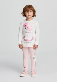 Maglietta bianca a maniche lunghe con un fiocco rosa e una grafica di un gatto, abbinata a leggings rosa chiaro con design di gatti e dettagli a forma di cuore. Materiale morbido.