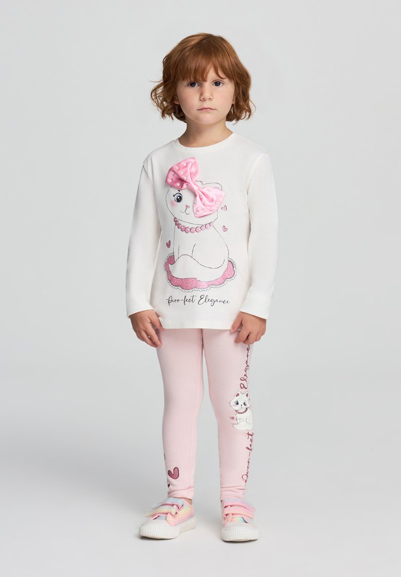 Maglietta bianca a maniche lunghe con un fiocco rosa e una grafica di un gatto, abbinata a leggings rosa chiaro con design di gatti e dettagli a forma di cuore. Materiale morbido.