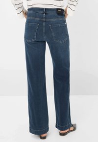 Dunkelblaue weit geschnittene Jeans aus Denim, mit hoher Taille, Gesäßtaschen und einem markierten Bund. Glatte Textur mit dezenten Nähten.
