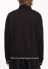 Sudadera negra con cuello alto, con un patrón de ramas blancas en el dobladillo inferior y puños acanalados. Textura suave y corte relajado.