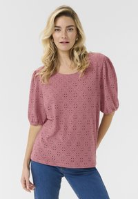 Top rosa ricamato con maniche a palloncino corte, caratterizzato da un motivo a diamante e un design a occhio, abbinato a jeans blu.