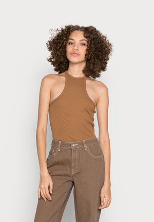 Top halter castanho com relevo e ombros à mostra, combinado com calças castanhas de cintura alta com costuras brancas e bolsos frontais.