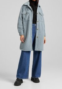 Light blue fleece coat with a collar, two chest pockets, and button closure, paired with high-waisted denim flared jeans and chunky black shoes.