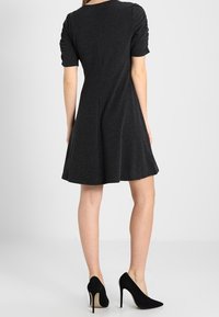 Zwart korte mouwen jurk met een getailleerde bovenkant en een uitlopende rok, gemaakt van een textuurstof, met geplooide details op de schouders.