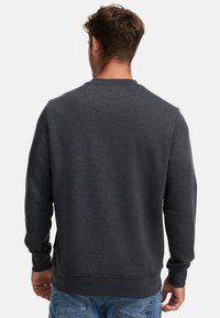 Dunkelgrauer Pullover mit rundem Ausschnitt, langen Ärmeln und gerippten Bündchen. Glatte Textur und figurbetontes Design mit minimaler Detailgestaltung.