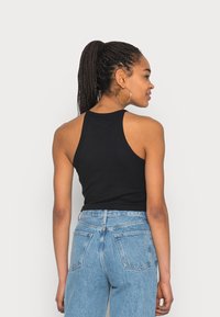 Top de alças preto canelado com um design de costas nadador. Combinado com jeans de cintura alta de tom azul claro. Modelo de costas para a câmara.
