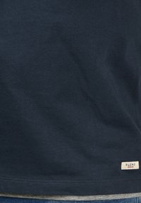 Polo majica tamnoplave boje od pamuka, s glatkom teksturom, koja na rubu ima malu bijelu oznaku s natpisom "BLEND DENIM". Jednostavan, klasičan dizajn.
