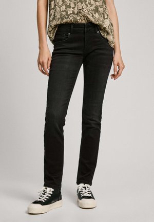 Femme portant un jean noir slim, des baskets noir et blanc, et un haut à manches courtes à motif floral.