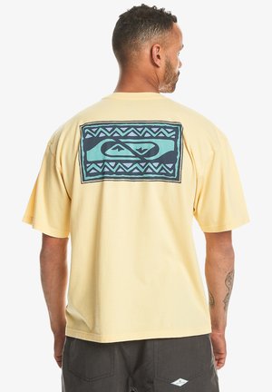 Yellow cotton t-shirt with short sleeves, featuring a large blue and black geometric design on the back. Relaxed fit with a round neckline.