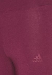Purple athletic leggings made of soft, stretchable fabric. Features a subtle texture and a small white adidas logo at the lower left.