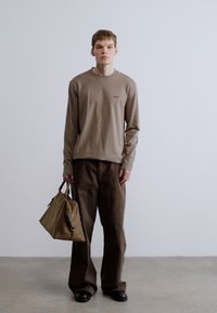 Hosszú ujjú, gesztenyebarna felső, barna, széles szárú nadrág és barna táska. Simogató anyag, egyszerű dizájn, minimalista logórészlet a felsőn.