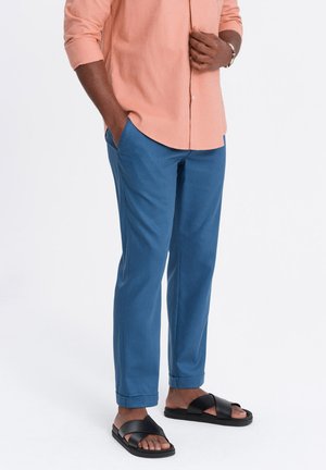 Blaue Chinos mit schmaler Passform, aus weichem Stoff, mit glatter Textur und umgeschlagenen Säumen, kombiniert mit schwarzen Riemchensandalen.