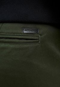 Ciemnozielony materiał o gładkiej fakturze, z tylną kieszenią, a także czarną skórzaną metką wytłoczoną napisem "JACK&JONES."