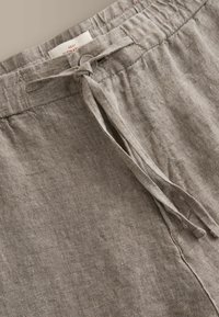 Pantalon en lin beige avec un cordon de serrage en tissu ajustable à la taille élastique et un détail de couture subtile.