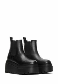 Black leather platform Chelsea boots with elastic side panels, rounded toes, and thick, ridged soles. Smooth texture and minimalist design.