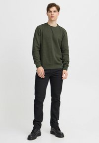 Olivengrøn bomulds sweatshirt med ribbede manchetter og kant, parret med sorte slim-fit jeans og sorte snørebåndsstøvler. Enkel, struktureret design.