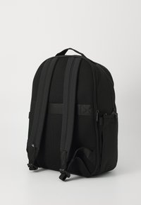 Sac à dos noir en tissu texturé, doté de bretelles en maille rembourrées, d'une poignée supérieure et de poches latérales pour le rangement. Fermeture à glissière lisse.