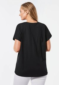 Schwarzes Baumwoll-T-Shirt mit kurzen Ärmeln, weitem Ausschnitt und lockerer Passform. Die Rückseite ist glatt, ohne sichtbare Marken oder Muster.