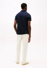 Polo shirt navy a maniche corte, abbinato a pantaloni bianchi e sneakers chiare, visto da dietro. Tessuto morbido, design aderente.
