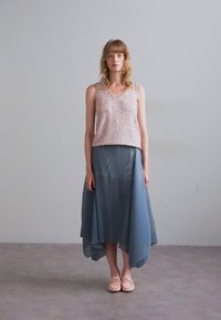Light pink sequin tank top paired with a blue pleated asymmetrical skirt. The model wears soft pink slip-on shoes, standing on a neutral floor.
