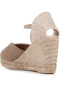 Brown suede wedge shoe with a woven beige fabric back. Features a textured jute midsole and ankle strap for secure fit.