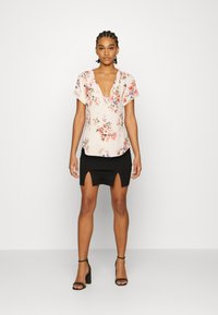 Blusa de cor-de-rosa clara com padrão floral e decote em V profundo, combinada com uma saia curta preta com fendas frontais. Sandálias pretas de salto.