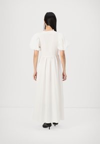 Vit maxiklänning med puffärmar, samlad midja och en flödande kjol. Bärs med svarta klackskor. Slät tygtextur.