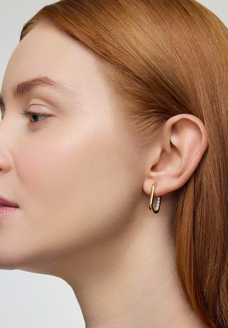 Złota kolczyk w kształcie obręczy z polerowaną powierzchnią, zdobiona rzędem przezroczystych kryształków wzdłuż przedniej krawędzi. Prosty, zaokrąglony design.