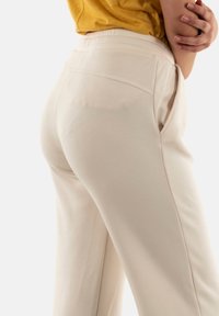 Pantalones beige de talle alto con bolsillos laterales, hechos de una tela ligera, que presentan una textura suave y un diseño de pierna recta.