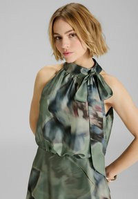 Top halter in satin verde con motivo floreale astratto blu e bordeaux. Presenta un fiocco legato al collo e una consistenza morbida e fluida.