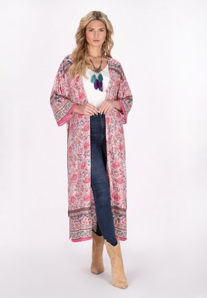Rosa, floral gemusterter Kimono mit weiten Ärmeln und kontrastierenden Säumen, kombiniert mit einem weißen Oberteil und dunklen Jeans, getragen mit hellbraunen Stiefeln.