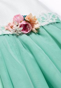 Un vestito verde menta con una parte superiore bianca testurizzata e una gonna in tulle a strati, caratterizzato da decorazioni floreali e dettagli in pizzo intricati.