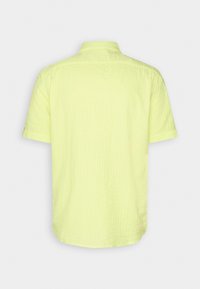 Krótki rękaw, żółta koszula z fakturowanej tkaniny, klasycznym kołnierzykiem i lekko zaokrąglonym dołem; wykonana z lekkiego materiału.