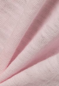 Miękka różowa dzianina o delikatnym, subtelnym splocie z subtelnymi cieniami podkreślającymi fakturę i fałdy.