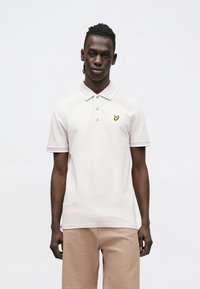 Lichtroze poloshirt met kraag, drieknopsbies en een klein geel geborduurd logo. Gemaakt van katoen met korte mouwen.